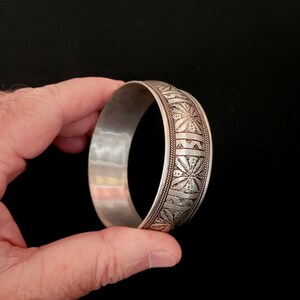 May include: A silver bangle bracelet with an intricate floral design. The bracelet is made of metal and has a smooth, polished finish.