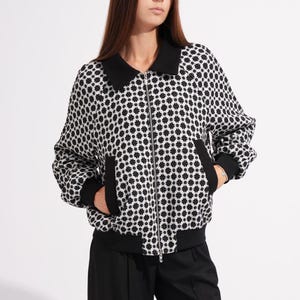 May include: A black and white patterned bomber jacket with a black collar and cuffs, paired with black wide-leg trousers. The jacket features a zipper closure and pockets. The outfit is a modern, stylish ensemble.