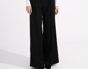 May include: A woman wearing a white long-sleeve top with a square neckline and black wide-leg trousers. The trousers have pleats at the waist. The outfit is simple and elegant, suitable for business or casual wear.