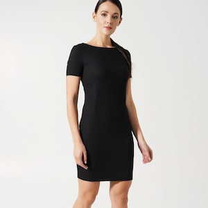 May include: A solid black short-sleeved dress featuring a boat neckline and a fitted silhouette that ends above the knee. The garment is constructed with vertical seams along the torso and is paired with black high-heeled pumps.