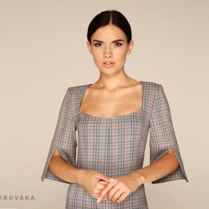 May include: A woman wearing a gray and red plaid dress with a square neckline and short sleeves. The dress has a fitted silhouette and a slightly flared skirt.