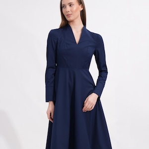 May include: A solid navy blue midi dress featuring long sleeves with wide cuffs, a structured bodice with vertical seam detailing, and a V-neckline. The skirt has a flared silhouette that falls below the knees, creating a clean and simple look.