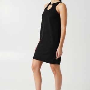 May include: A black sleeveless dress with a heart-shaped cutout at the neckline. The dress has a simple, fitted silhouette and falls just above the knee.