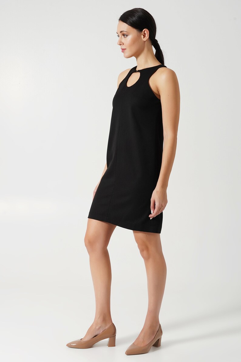 May include: A black sleeveless dress with a heart-shaped cutout at the neckline. The dress has a simple, fitted silhouette and falls just above the knee.