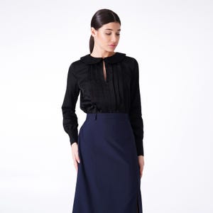 Peut inclure: Un chemisier noir à manches longues avec un col Claudine et une ouverture en forme de trou de serrure au niveau du décolleté. Le chemisier est associé à une jupe midi bleu foncé.