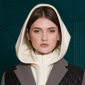 May include: A woman wearing a white hooded jacket over a gray and black quilted jacket. The jacket has a zipper closure and a quilted design.