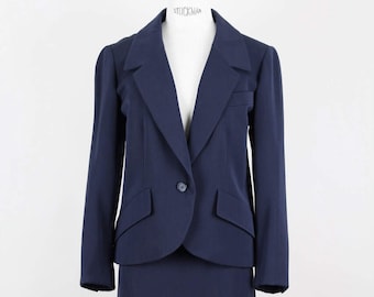 May include: A navy blue blazer and skirt suit. The blazer has a single button closure and a notched collar. The skirt is knee-length.