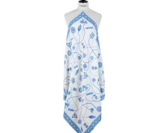 May include: A white scarf with a blue floral and abstract design. The scarf is draped over a mannequin and features a blue border. The pattern includes various shapes and lines in a delicate, artistic style.