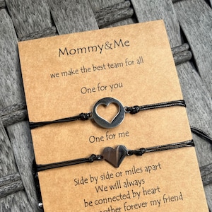 Puede incluir: Un conjunto de dos pulseras de amistad negras con dijes de corazón plateados. La tarjeta dice "Mommy & Me we make the best team for all One for you One for me Side by side or miles apart We will always be connected by heart First my mother forever my friend".