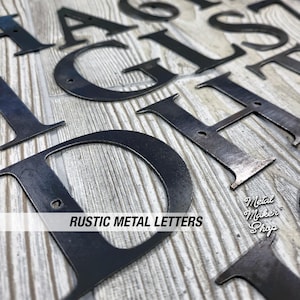May include: Close-up of various black metal letters, including A, D, G, and H, arranged on a light wood-grain surface. The letters have a rustic, weathered appearance. Text on the image reads "RUSTIC METAL LETTERS" and "Metal Maker Shop."