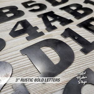 May include: A set of 3-inch rustic bold metal letters in various shapes, including A, B, D, and 1. The letters are black and have a rough, textured surface. The letters are arranged on a wooden surface. The text "3" RUSTIC BOLD LETTERS" is visible at the bottom of the image.