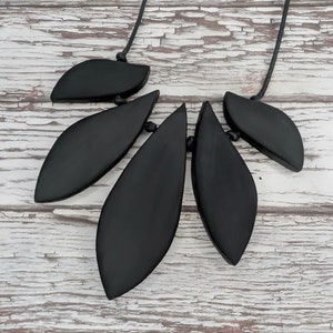 May include: Black wooden leaf necklace with a black cord. The necklace is made of five leaves, each with a different shape and size.