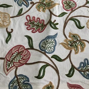 May include: White fabric with embroidered floral designs in shades of pink, blue, green, and beige. The design features intricate leaves and flowers with a vintage aesthetic.