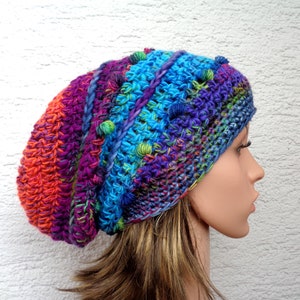 Può includere: Un berretto lavorato a uncinetto colorato con una vestibilità morbida e un design testurizzato. Il berretto è realizzato con una varietà di colori, tra cui arancione, viola, blu e verde. Il berretto ha un pon pon sulla cima.
