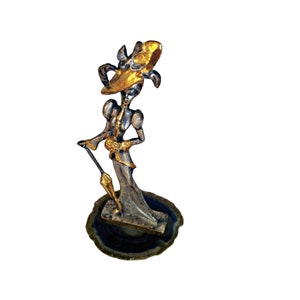 May include: A silver and gold figurine of a woman wearing a large hat and holding an umbrella. The figurine is standing on a blue and white agate base.