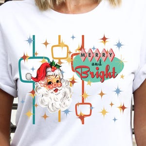 May include: White t-shirt with a retro design featuring a Santa Claus illustration, a turquoise sign with the text "Merry and Bright", and gold stars.
