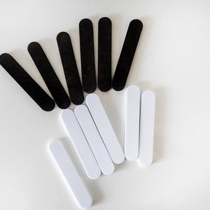 May include: A collection of black and white nail files arranged on a white surface. The files are rectangular with rounded ends, and are likely used for manicure or pedicure nail care.
