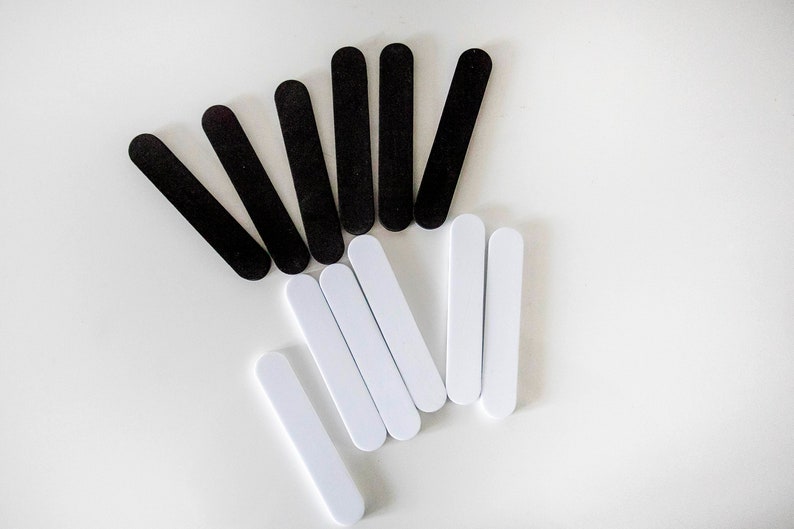 May include: A collection of black and white nail files arranged on a white surface. The files are rectangular with rounded ends, and are likely used for manicure or pedicure nail care.