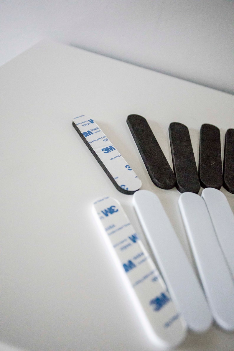 May include: An assortment of black and white adhesive strips, some with 3M branding. The strips are rectangular with rounded ends, designed for mounting or securing items. The image is taken from a high angle.