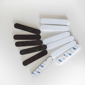May include: An assortment of black and white rectangular adhesive strips. The black strips have a textured surface, while the white strips are smooth. Several strips have 3M double-sided tape attached.