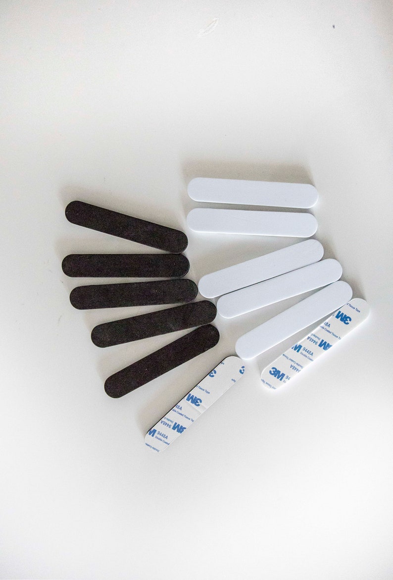 May include: An assortment of black and white rectangular adhesive strips. The black strips have a textured surface, while the white strips are smooth. Several strips have 3M double-sided tape attached.