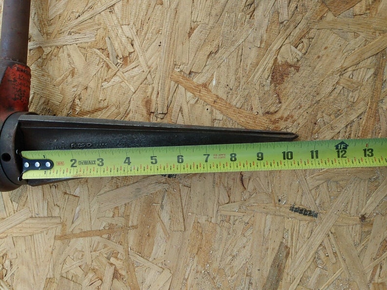 May include: A close-up of a metal tool with a yellow measuring tape. The tool is 13 inches long and has a black handle. The tool is on a wood surface.