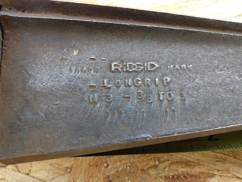 May include: Close-up of a metal tool with the text "RIDGID MARK LONG-RIP IN 3 7/8 TO 10" engraved on the surface.