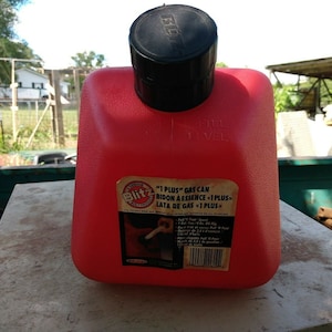 Peut inclure: Un bidon d'essence en plastique rouge avec un couvercle noir. Le bidon porte une étiquette indiquant "1 PLUS" gas can, bidon à essence <1 PLUS>, lata de gas <1 PLUS>. L'étiquette comporte également un code-barres.