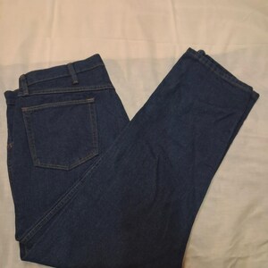 May include: Dark blue denim jeans with a classic five-pocket design. The jeans are folded and laid flat, showing the back pockets and the straight leg cut. The fabric appears to be a medium-weight denim.