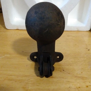 May include: A black cast iron furniture caster with a round ball top and a single wheel. The caster is designed to be attached to a piece of furniture.