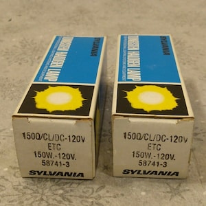 Puede incluir: Dos cajas blancas con acentos azules y amarillos. Las cajas contienen bombillas halógenas Sylvania 1500/CL/DC-120V ETC 150W.-120V. 58741-3.