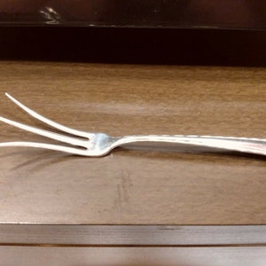 May include: A silver four-pronged fork with a slightly curved handle.