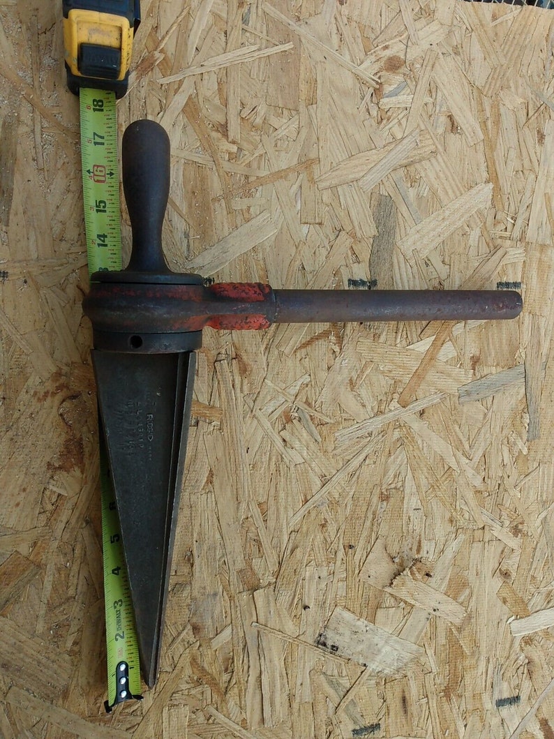 May include: A rusty metal pipe threading tool with a wooden handle and a measuring tape in the background.