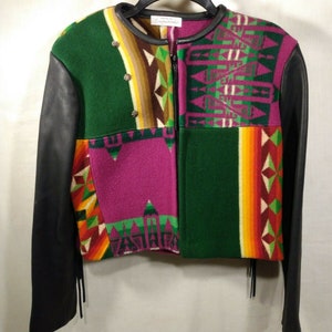 May include: A green, pink and orange patterned jacket with black leather sleeves and a zip closure. The jacket has fringe details on the sleeves and bottom.