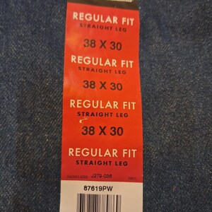 May include: A red tag for Rustler jeans, with the text "REGULAR FIT STRAIGHT LEG" and size "38 X 30". The tag also includes a barcode and the text "87619PW". The tag is on a blue denim background.