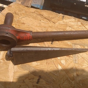May include: A rusty, red and black pipe wrench with a long handle and a wedge-shaped tool. The tools are on a wooden surface.