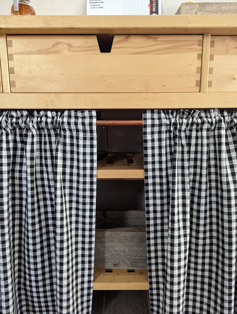 May include: A wooden cabinet with a drawer and open shelves. The shelves are covered with black and white checkered curtains.