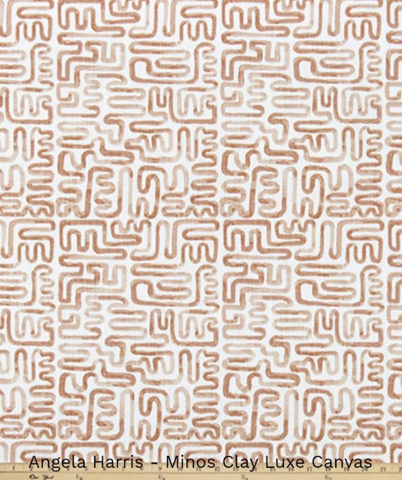 May include: A fabric with a repeating pattern of abstract, brown, squiggly lines on a white background. The fabric is labeled "Angela Harris - Minos Clay Luxe Canvas". The design is reminiscent of ancient symbols.