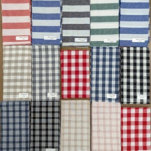 May include: A collection of 15 fabric swatches in various patterns and colors, including red, blue, black, green, tan, and white. The swatches are arranged in three rows of five. The fabric patterns include stripes, gingham, and plaid.
