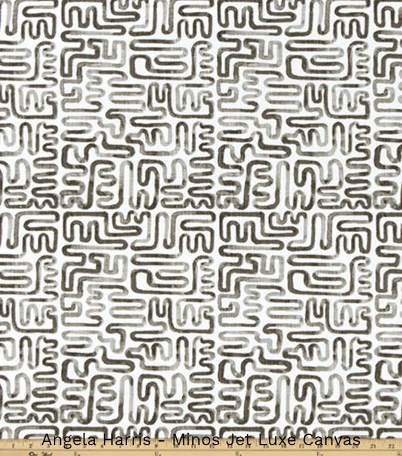 May include: White fabric with a repeating pattern of dark gray, abstract shapes. The fabric has a textured appearance. The text "Angela Harris - Minos Jet Luxe Canvas" is printed at the bottom.