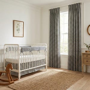 Puede incluir: Una habitación infantil con una cuna blanca con ropa de cama de cuadros vichy en blanco y negro y una falda a juego. La habitación incluye cortinas de cuadros vichy en blanco y negro, un caballito balancín de madera y una alfombra de fibra natural. Una impresión botánica enmarcada cuelga de la pared.