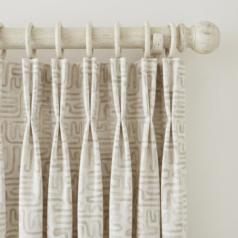 May include: Cream-colored curtain panels with a repeating geometric pattern in a light brown hue. The curtains are hung on a distressed white wooden rod with matching rings. The design creates a textured, layered effect.