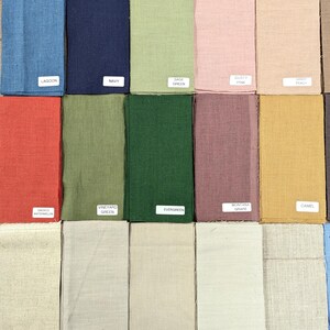 K&ouml;nnte beinhalten: Eine Sammlung von Stoffmustern in verschiedenen Farben, darunter Blau, Gr&uuml;n, Rosa und Beige. Jedes Muster hat ein Etikett mit einem Farbnamen, wie "Lagoon", "Navy" und "Evergreen". Die Stoffe scheinen aus Leinen oder einer &auml;hnlichen Naturfaser zu bestehen.