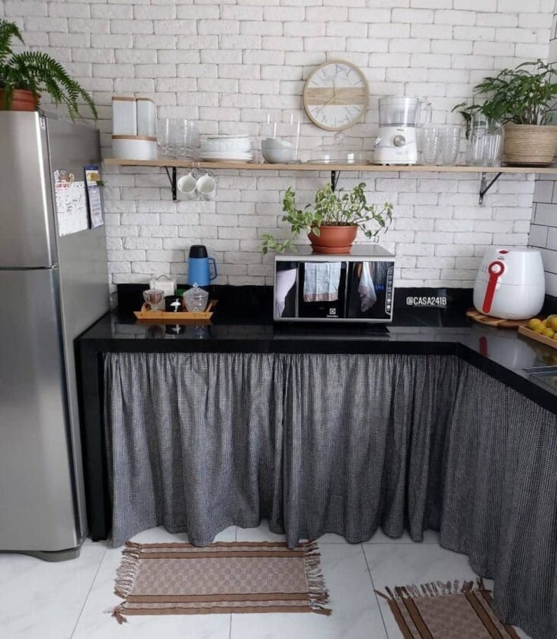 May include: A kitchen counter with a black countertop and a white brick backsplash. The counter has a microwave, an air fryer, and a coffee maker. The counter is decorated with a black and white checkered tablecloth and a brown rug.