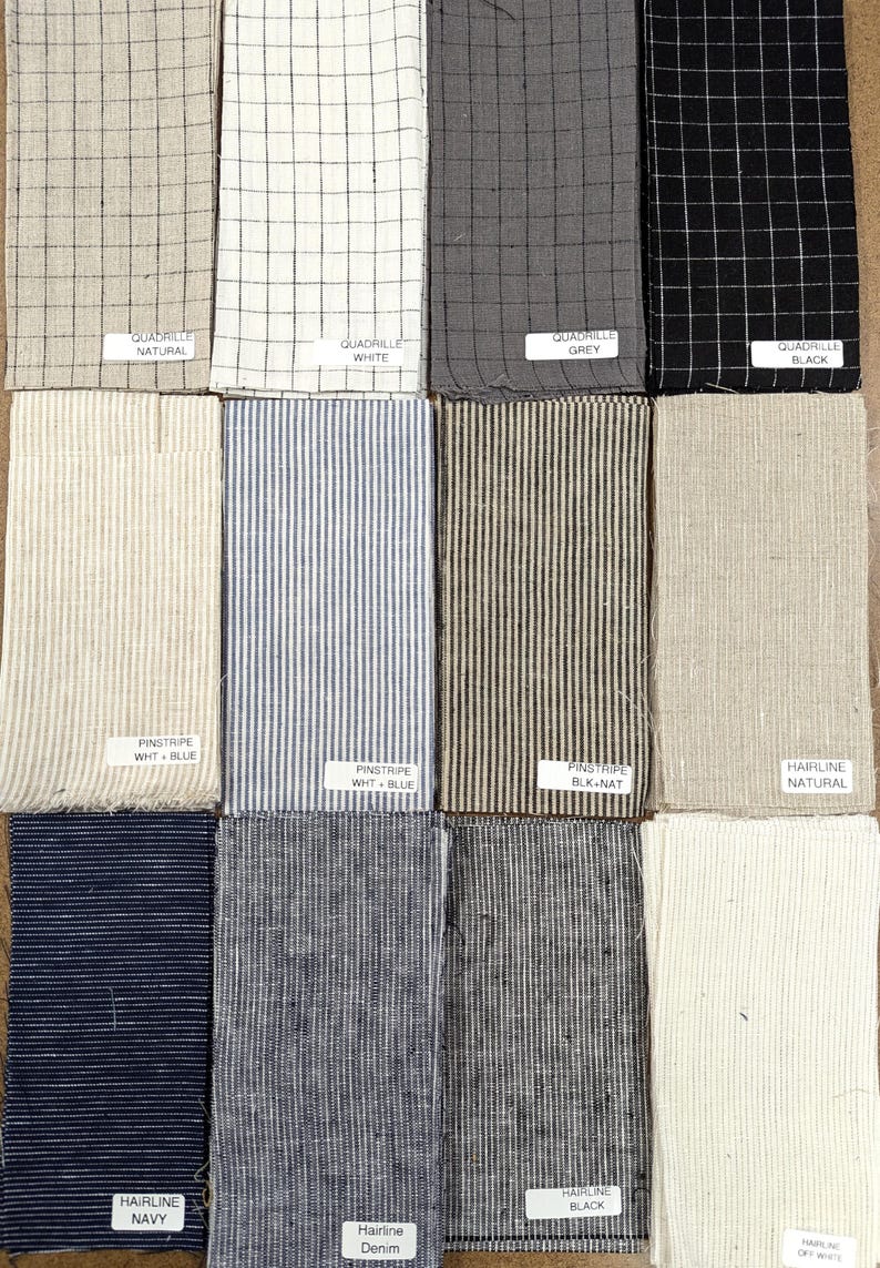 K&ouml;nnte beinhalten: Eine Sammlung von Stoffmustern in verschiedenen Mustern und Farben. Die Muster umfassen Gitter-, Nadelstreifen- und Haarlinien-Designs in Grau-, Schwarz-, Wei&szlig;-, Blau- und Naturt&ouml;nen. Jedes Muster hat ein Etikett mit dem Stoffnamen.