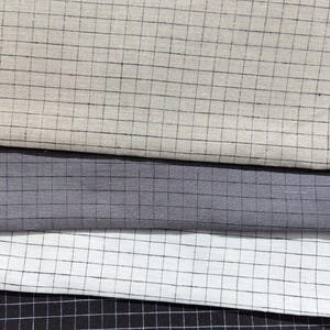 K&ouml;nnte beinhalten: Nahaufnahme von vier Stoffmustern in neutralen T&ouml;nen. Die Stoffe sind hellbeige, grau, wei&szlig; und schwarz, jeweils mit einem Rastermuster aus d&uuml;nnen schwarzen Linien. Die Stoffe sind &uuml;bereinander gestapelt.