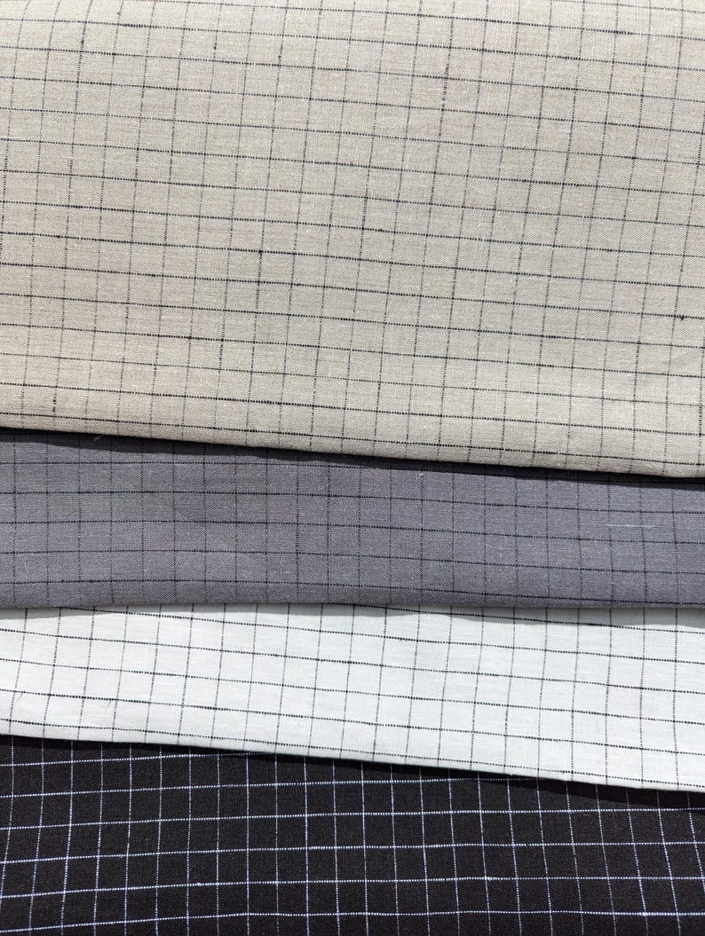 K&ouml;nnte beinhalten: Nahaufnahme von vier Stoffmustern in neutralen T&ouml;nen. Die Stoffe sind hellbeige, grau, wei&szlig; und schwarz, jeweils mit einem Rastermuster aus d&uuml;nnen schwarzen Linien. Die Stoffe sind &uuml;bereinander gestapelt.