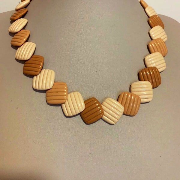 Collier de perles carrées beige crème et taupe avec des lignes texturées.