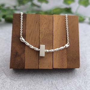 May include: A silver necklace with a twisted chain and a rectangular pendant.