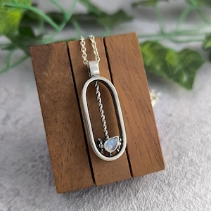 May include: A silver pendant necklace with an oval-shaped frame and a twisted rope design. The pendant features a small, iridescent opal gemstone.